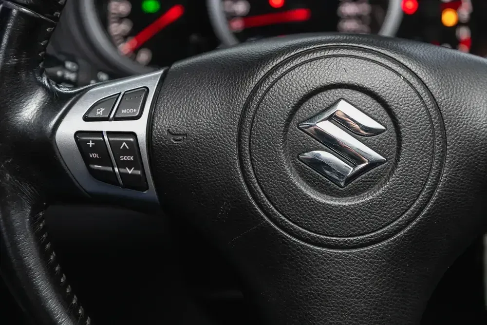 Close-up of a Suzuki steering wheel with control buttons and dashboard lights in the background