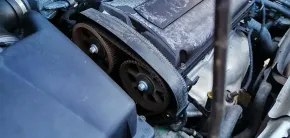 Car engine timing belt and pulleys exposed under the hood, with a black cover in the foreground