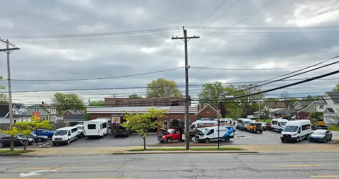 Busy roadside car lot with many parked vehicles under a cloudy sky