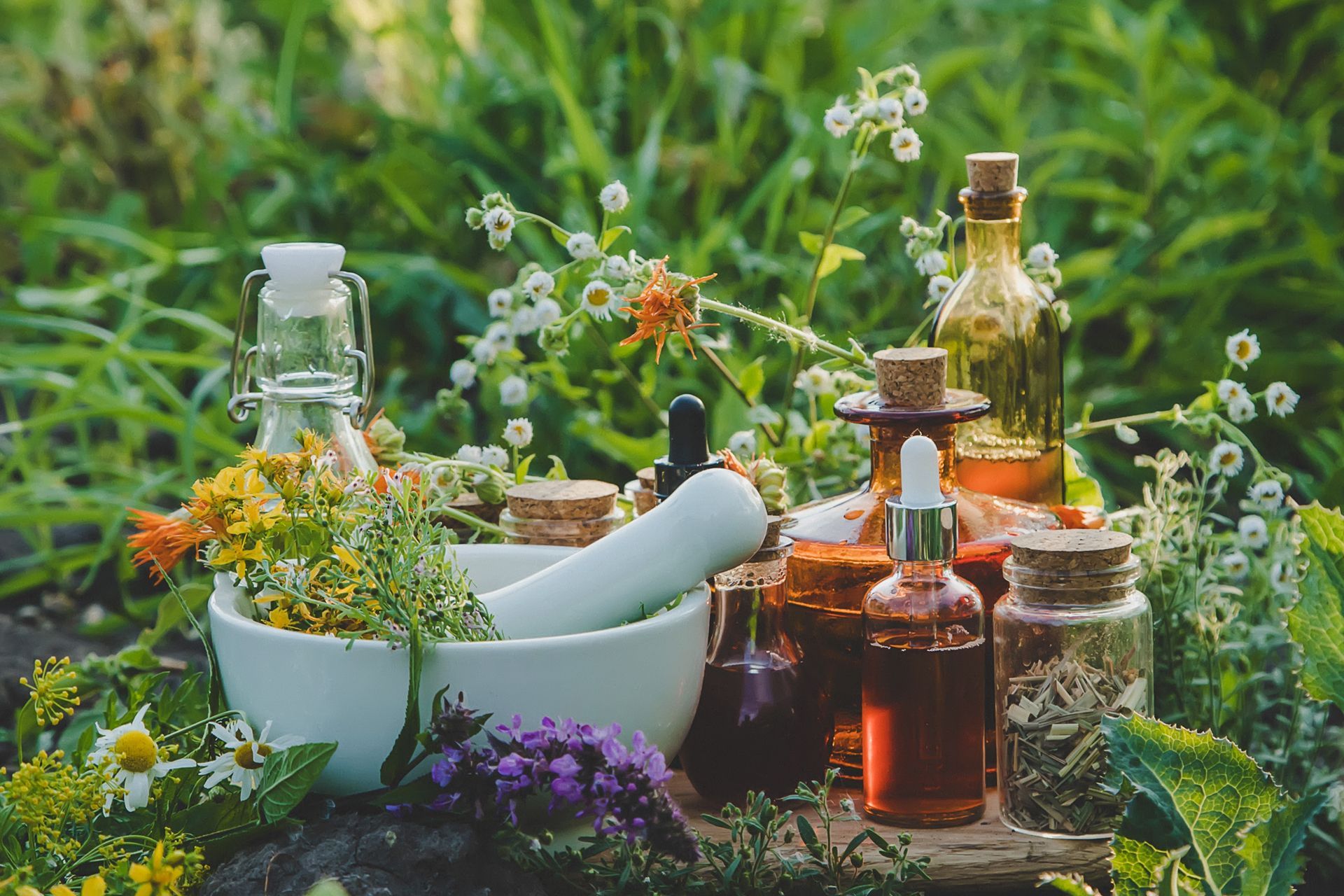 A mortar and pestle surrounded by bottles of essential oils and flowers.