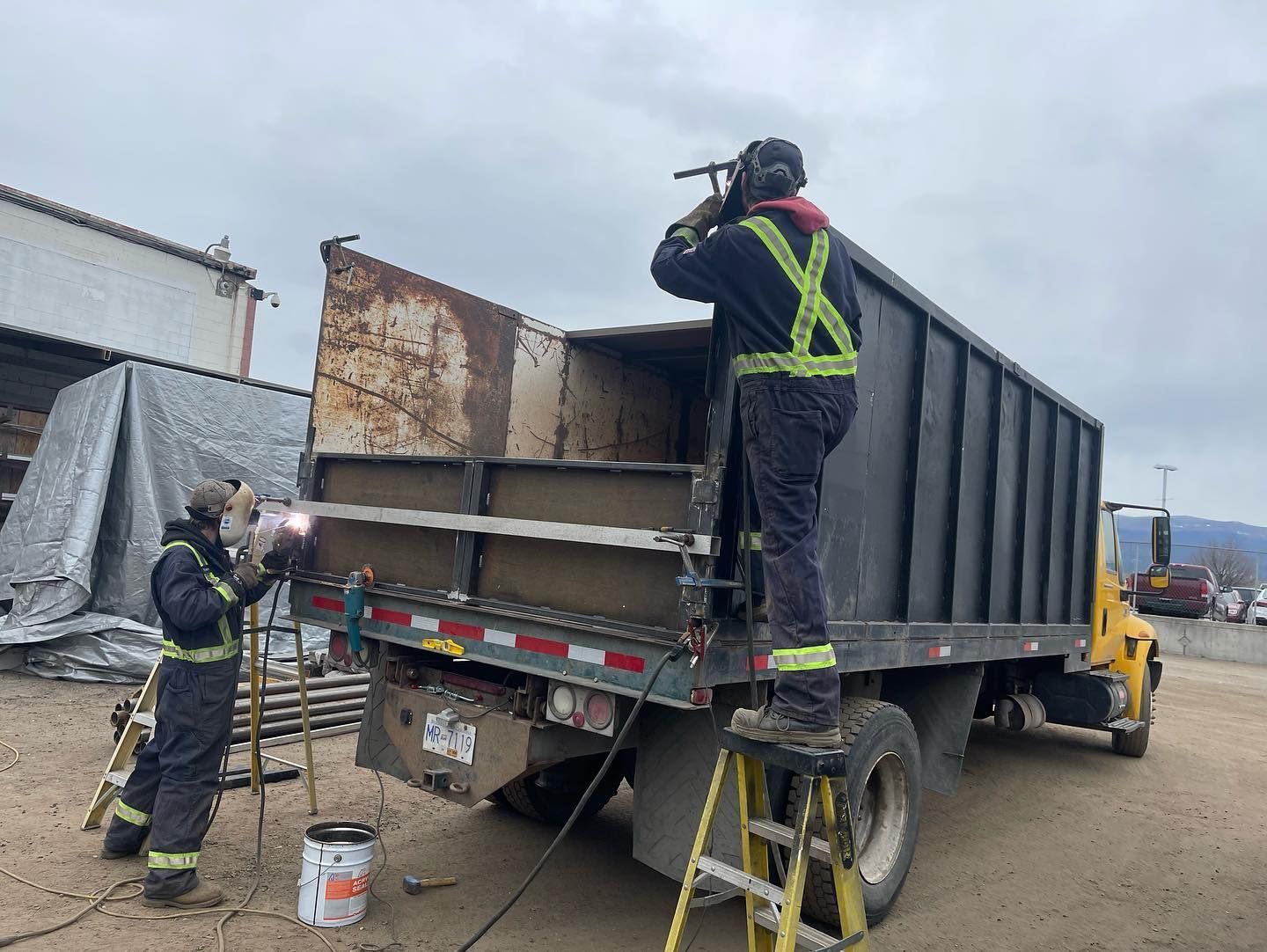 Two men are welding the back of a dump truck.