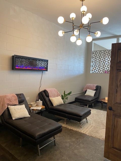 Modern lounge with two black chaise chairs, wall-mounted fireplace, chandelier, rug, and wooden partition