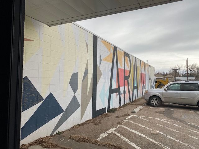 Colorful mural on a building wall beside a parked silver pickup in a lot under an overcast sky.