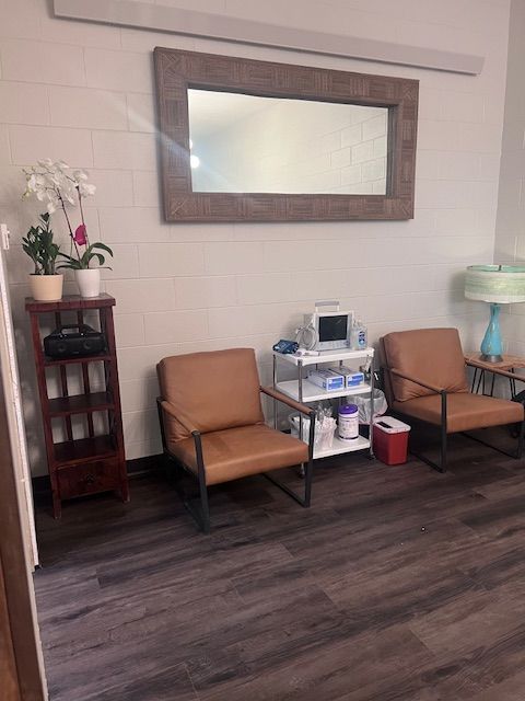 Waiting area with tan chairs, medical equipment, a mirror, and a small shelf in a tiled room.