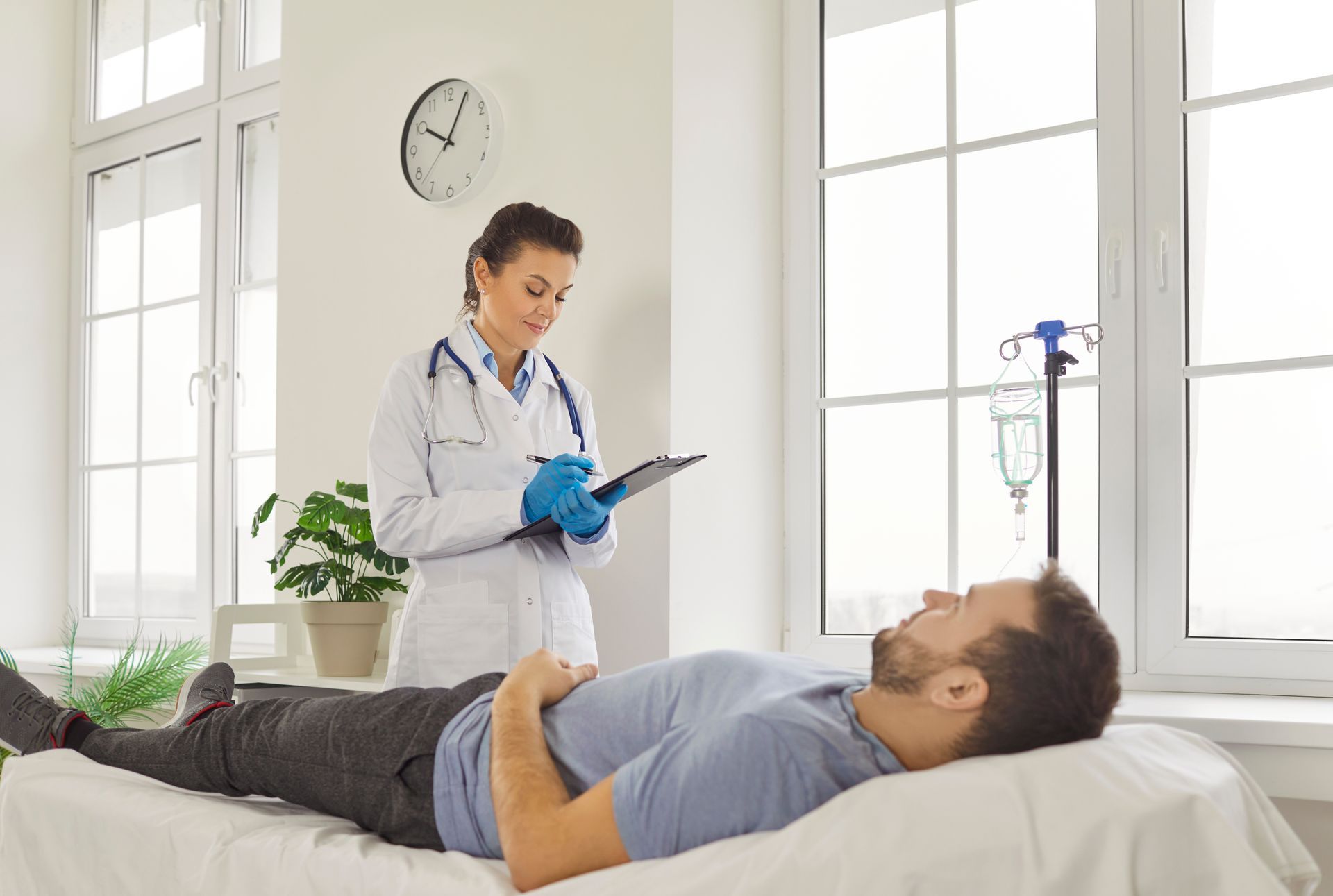 Doctor examining patient in a bright clinic room while he lies on an exam table