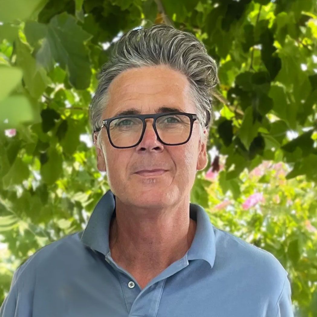 Ein Mann mit Brille und blauem Poloshirt steht vor einem Baum.