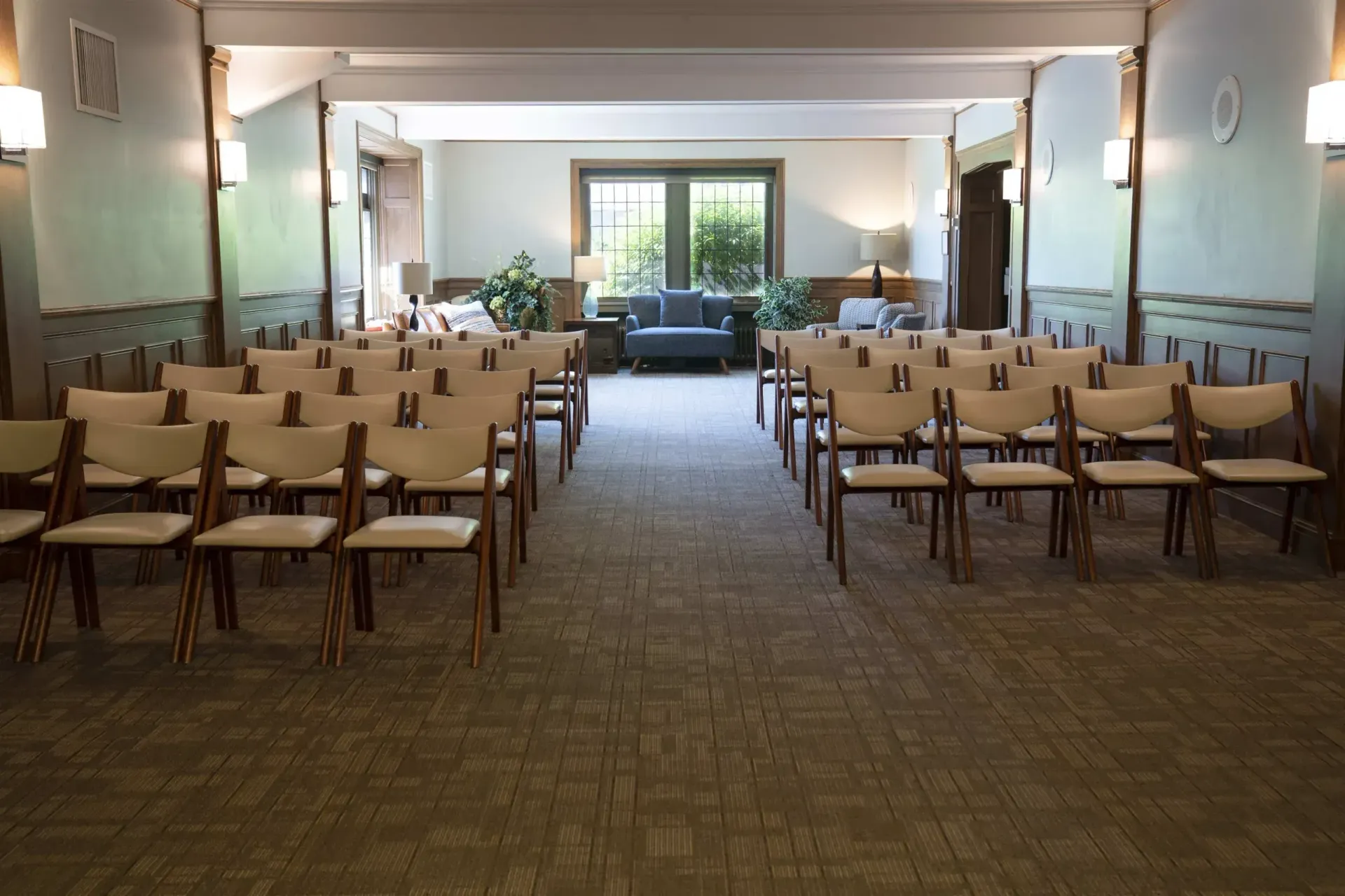 Empty conference room with rows of chairs facing a bright window at the far end.