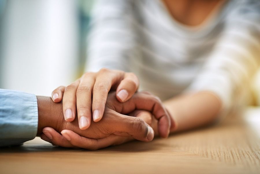 Two people holding hands across a wooden table in a close, comforting gesture