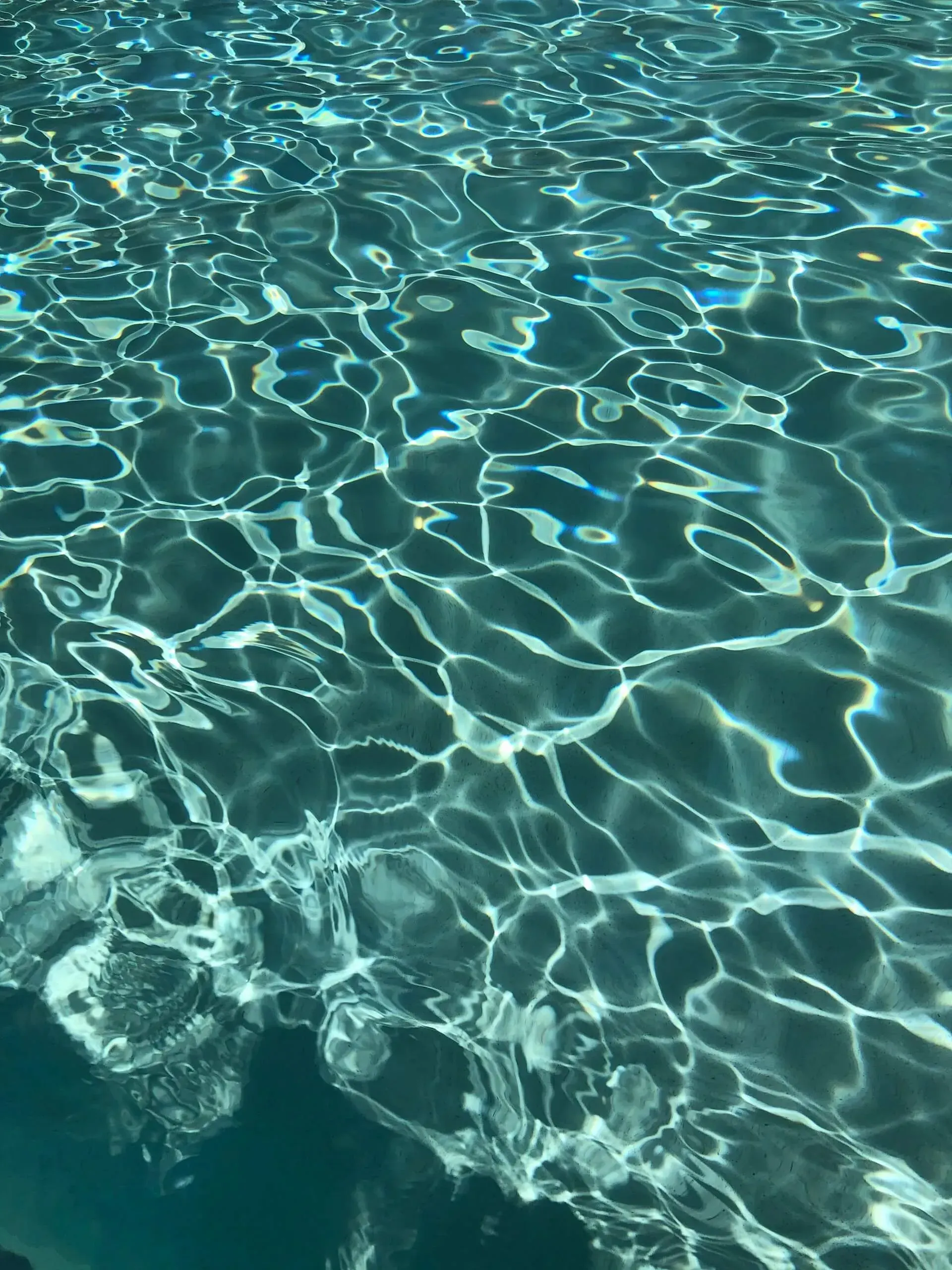 Sunlit ripples on clear turquoise pool water, with a splash at lower left