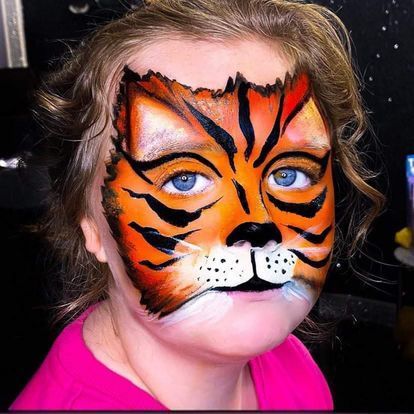 a little girl has her face painted like a tiger .
