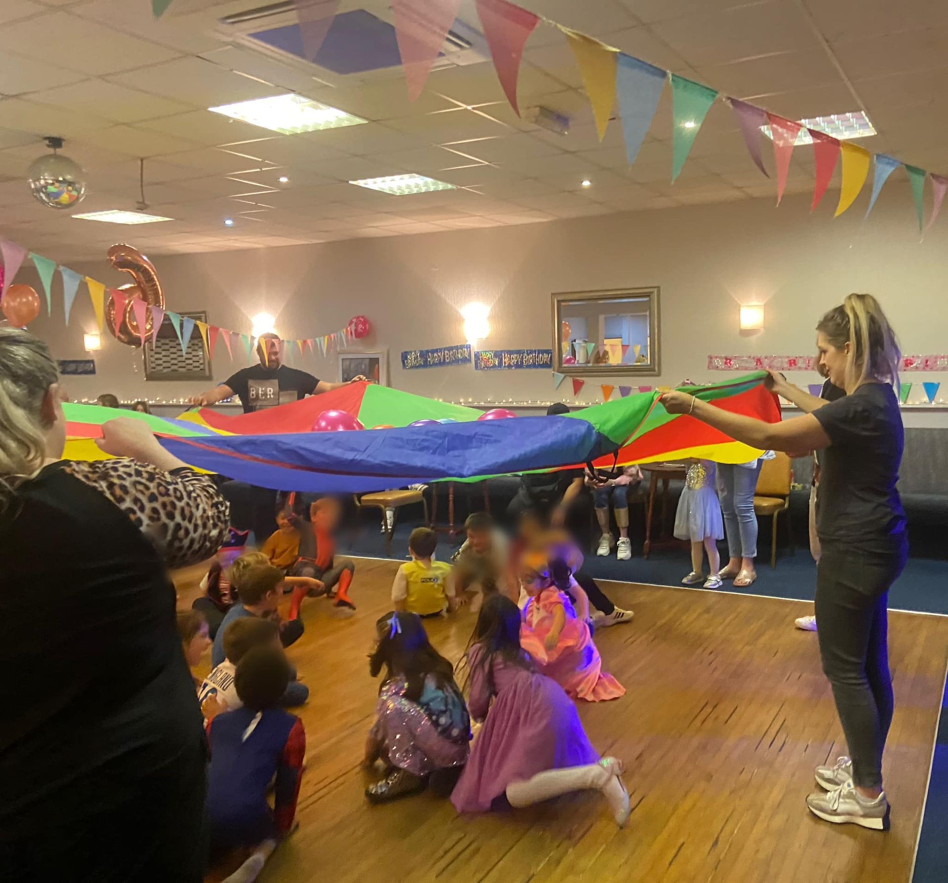 a woman is holding a colorful parachute over a group of children