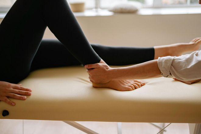 A person receiving foot massage on a massage table. The therapist holds the ankle, applying pressure.