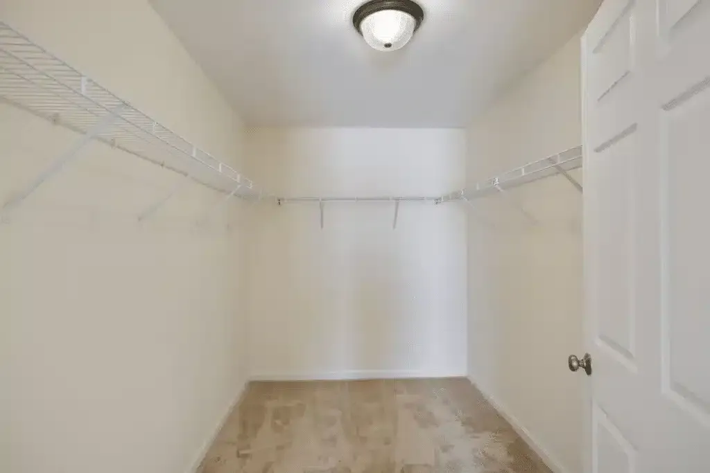 Empty walk-in closet with white wire shelves, beige walls, tiled floor, and an open door