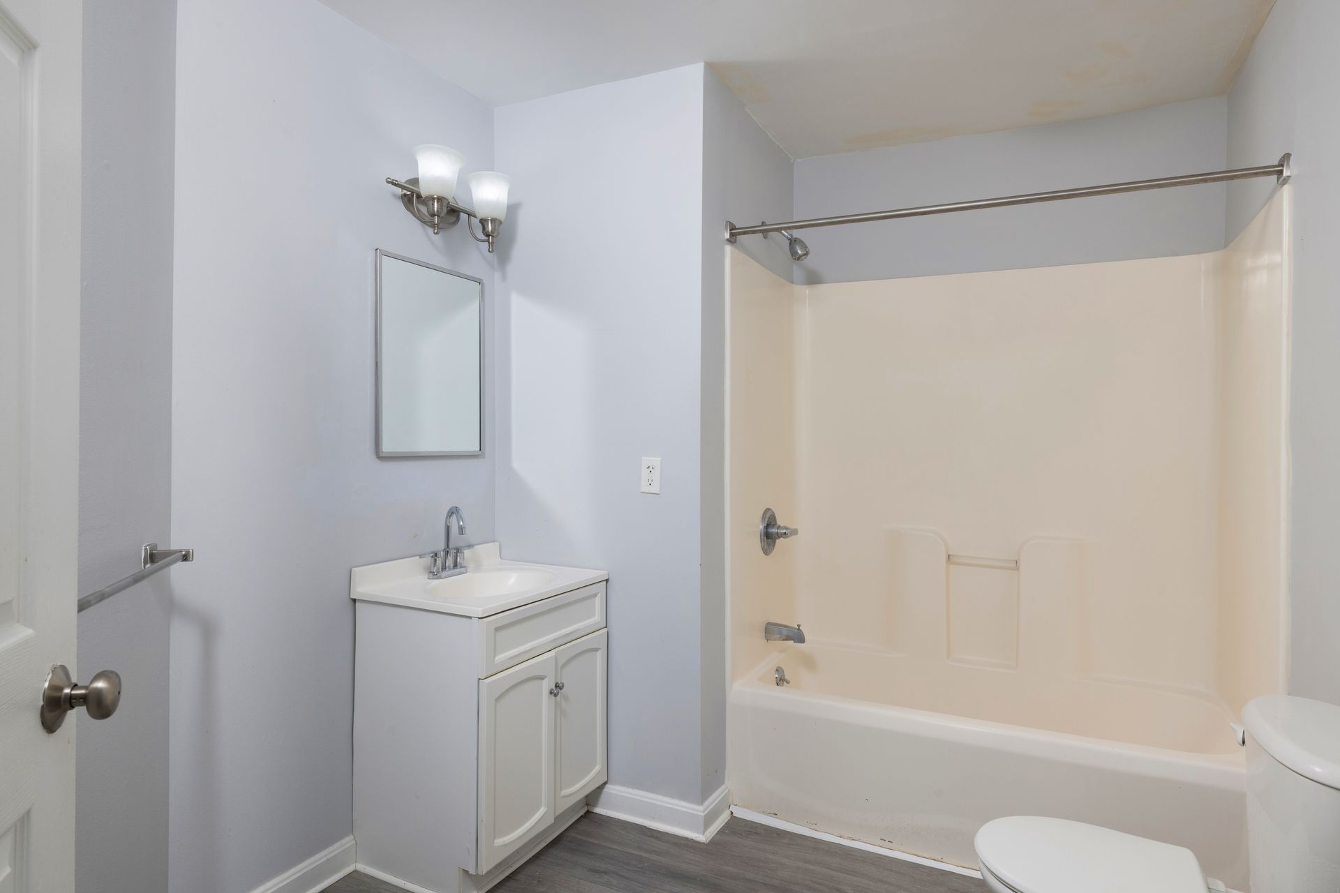 Small bathroom with vanity, mirror, wall sconce, and bathtub with shower curtain rod.