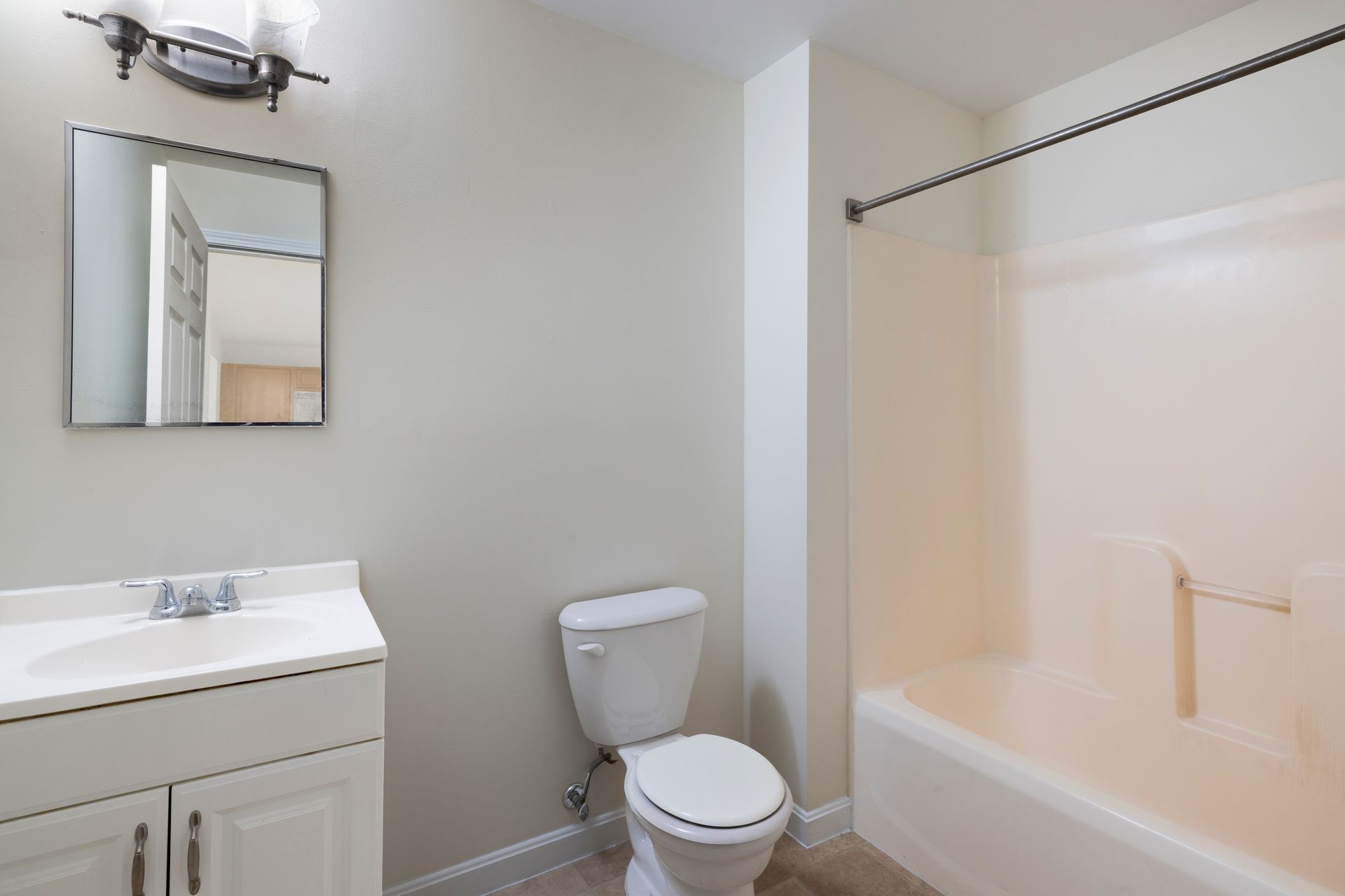 Small bathroom with white vanity, toilet, bathtub, and mirror against light gray walls.