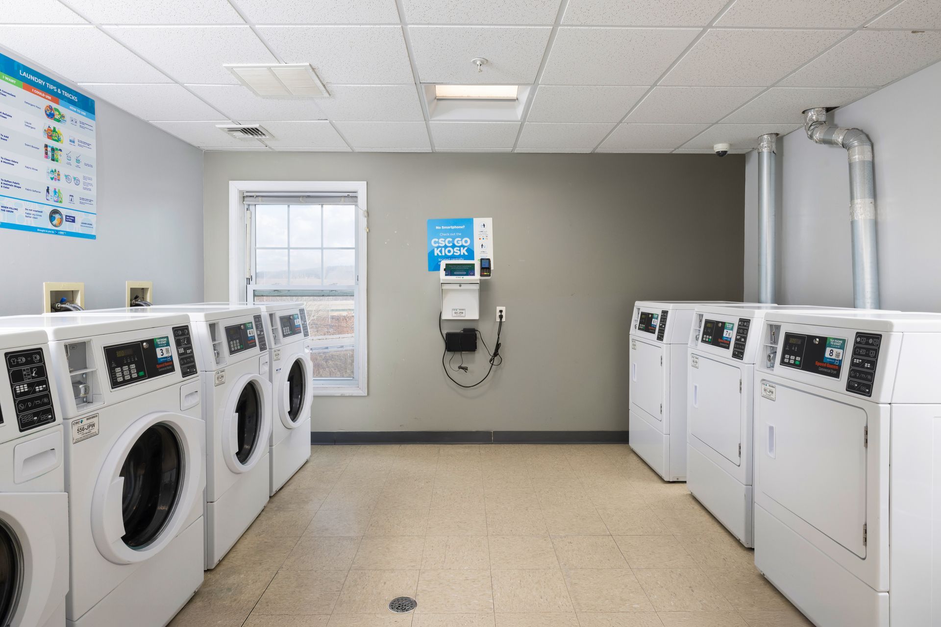 Laundry room with rows of white washers and dryers on both sides and a wall-mounted payment machine.