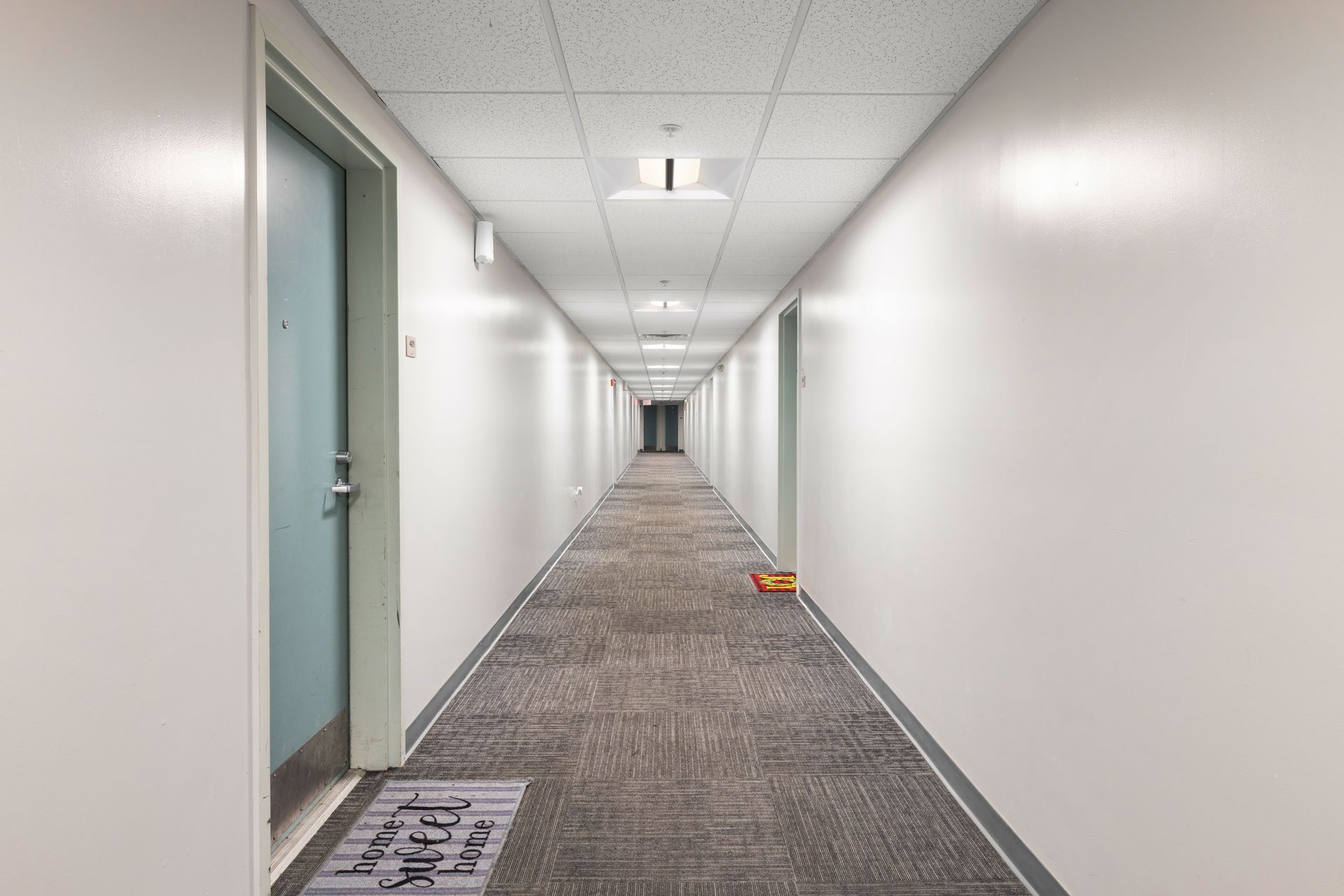 Long white office hallway with gray carpet, closed doors, fluorescent lights, and a small orange object on the floor.