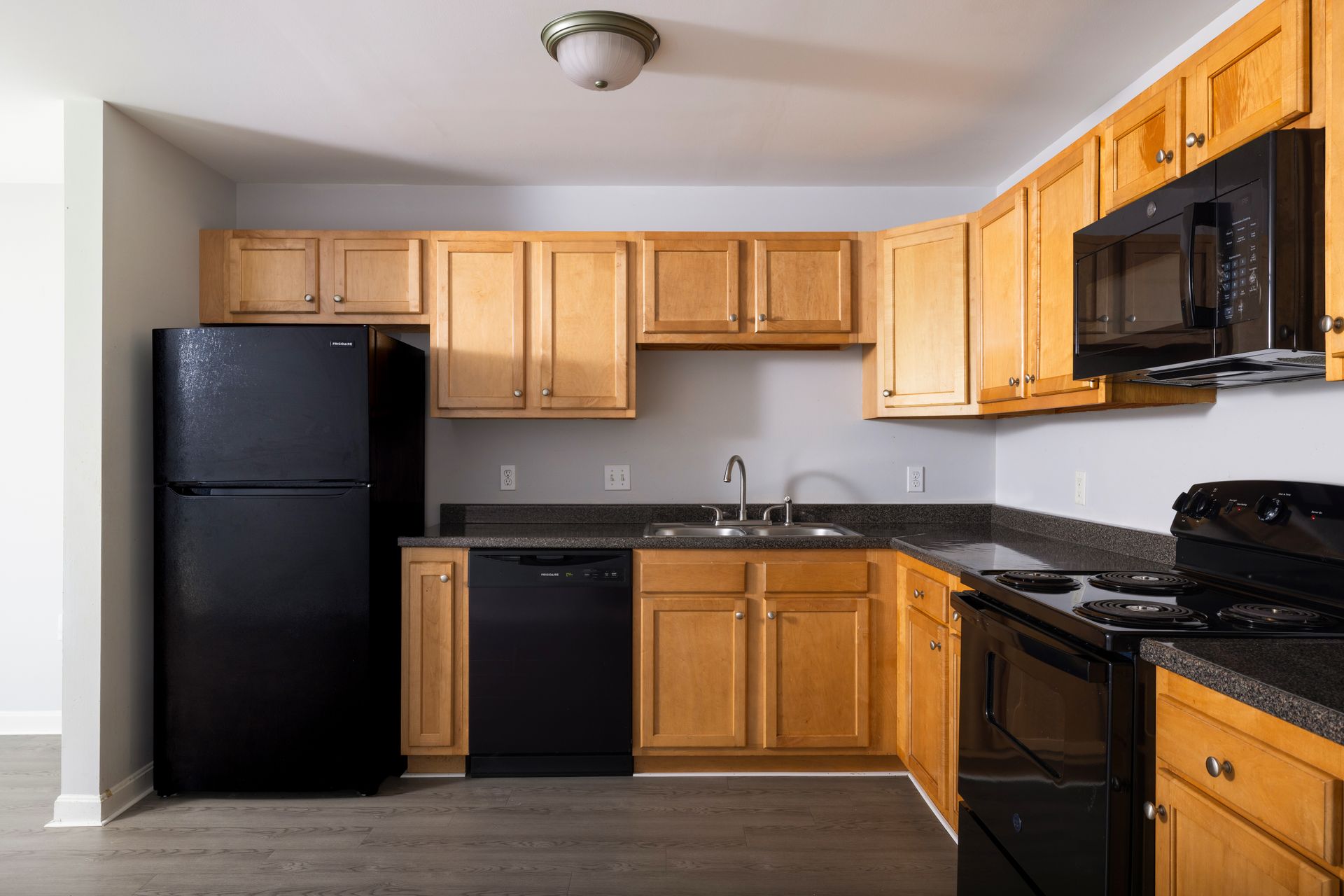 Modern kitchen with black appliances, light wood cabinets, and gray countertops