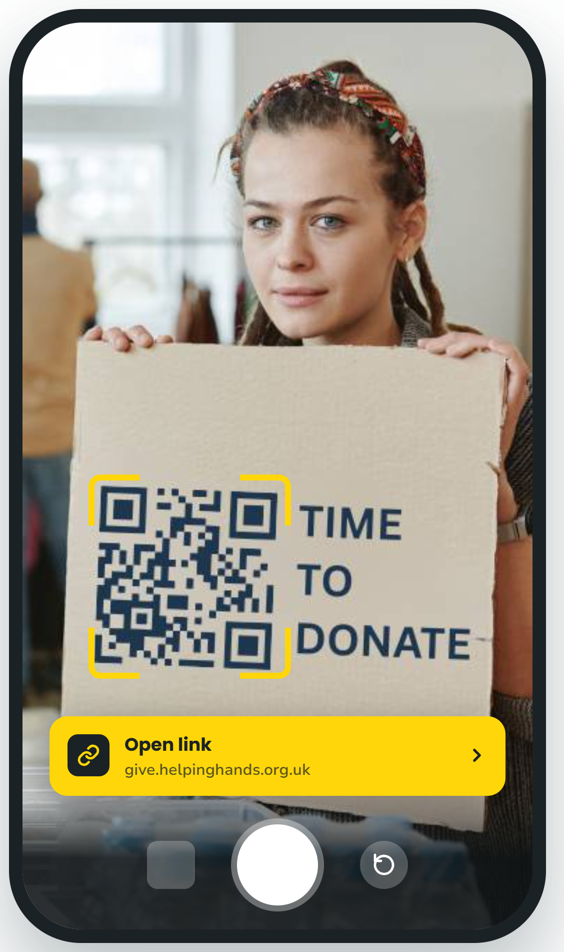 Person holding a donation sign with a QR code and the words “TIME TO DONATE” on a yellow app screen.