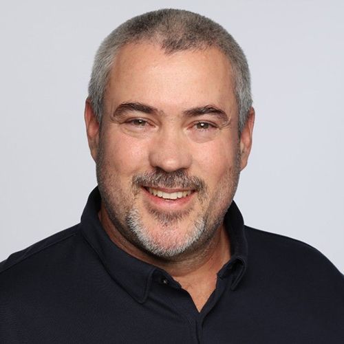 A man with a beard is smiling for the camera while wearing a black shirt.