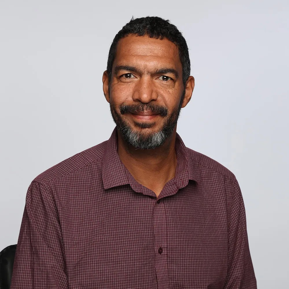 A man with a beard is wearing a plaid shirt and smiling for the camera.