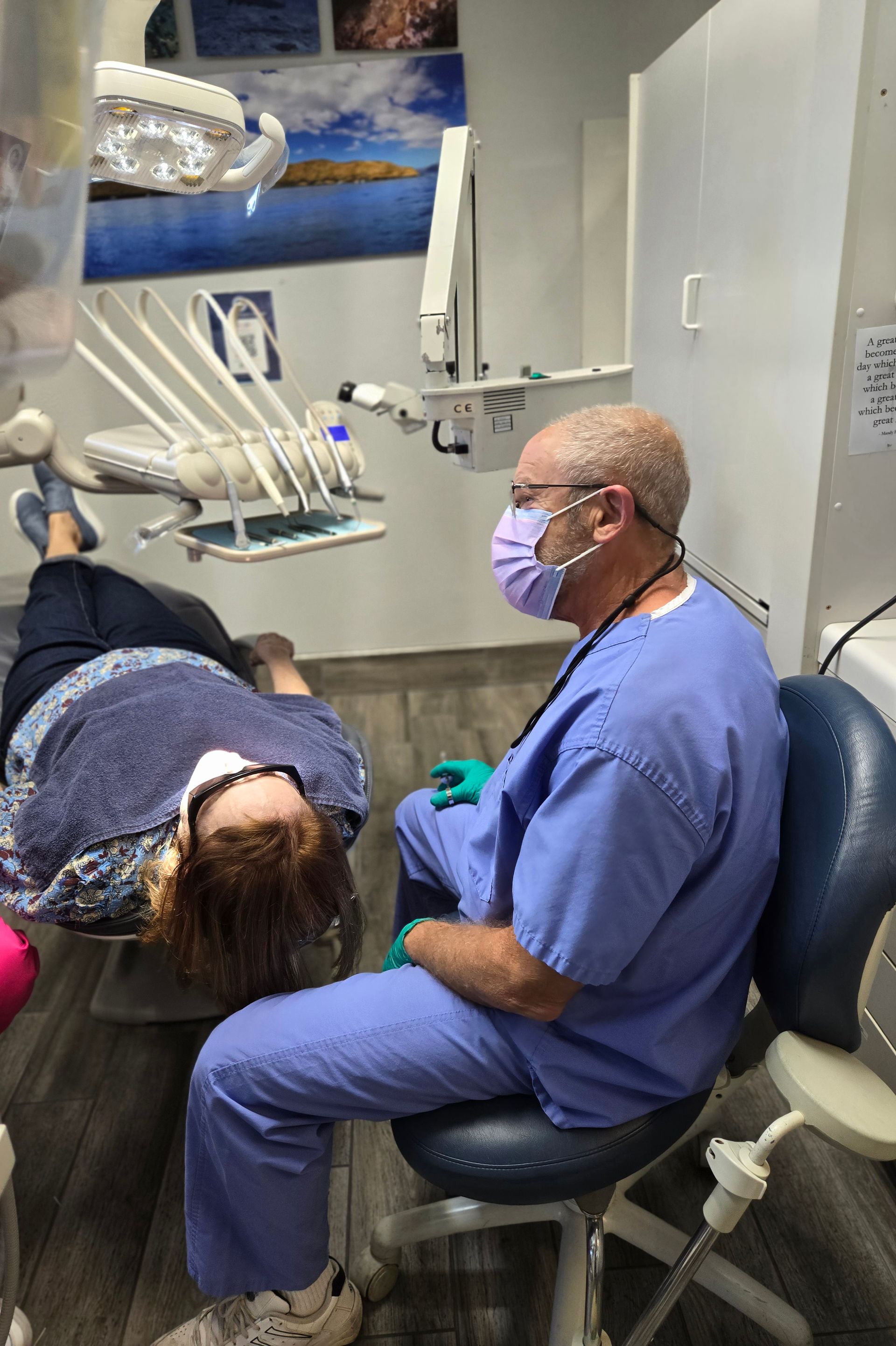 A dentist wearing a mask is sitting in a dental chair with a patient.