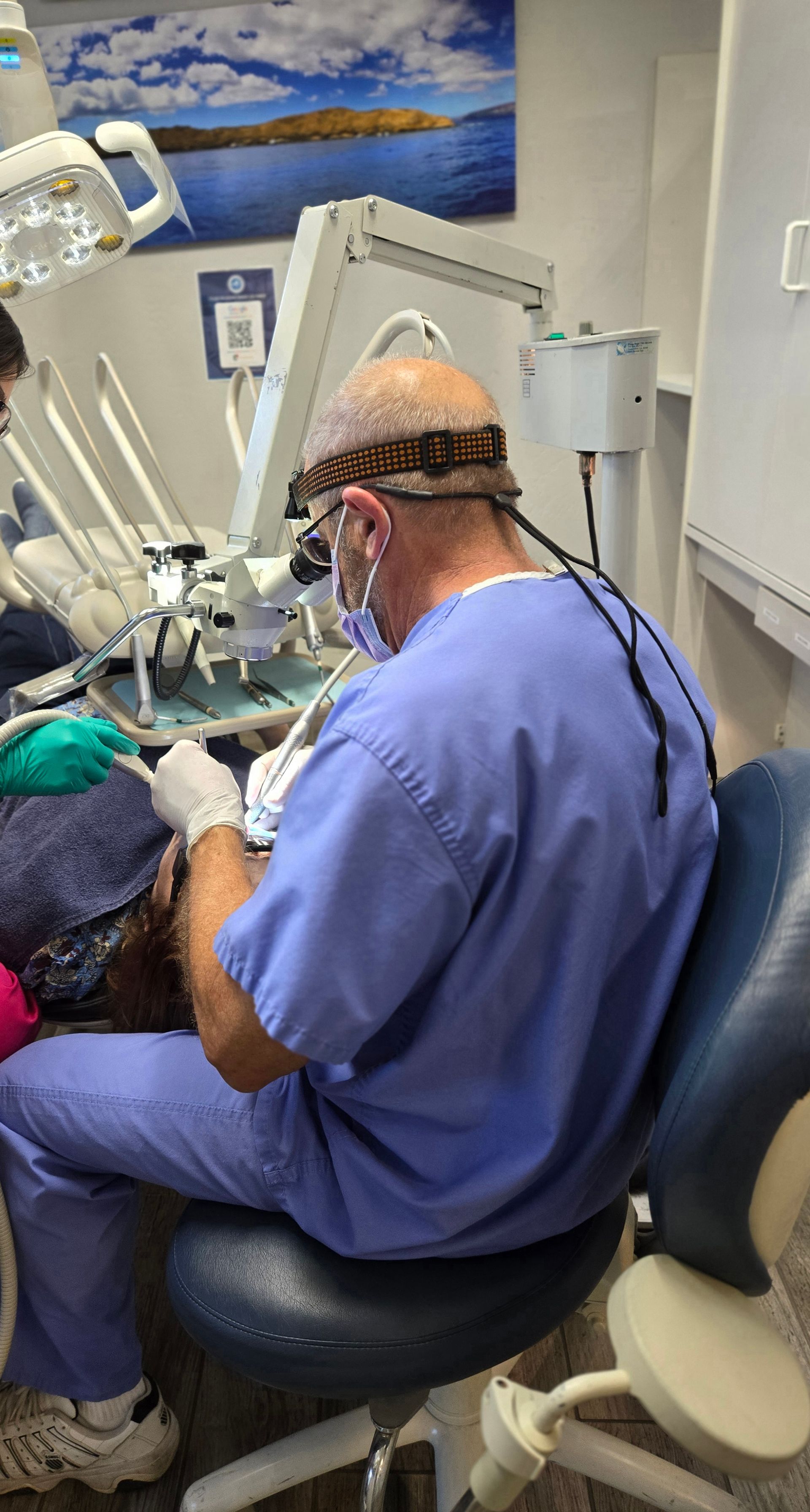 A dentist is sitting in a dental chair working on a patient.