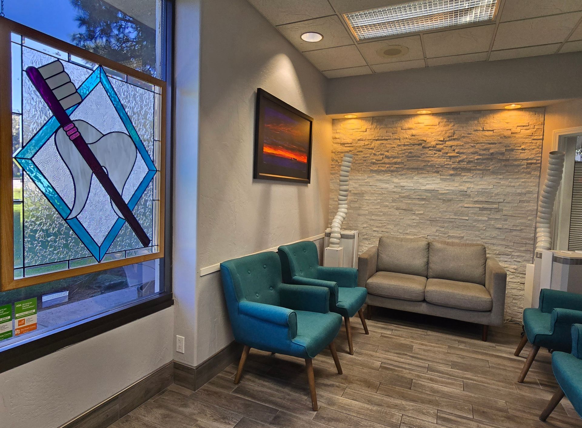 A dental office waiting room with a couch , chairs , and a stained glass window.