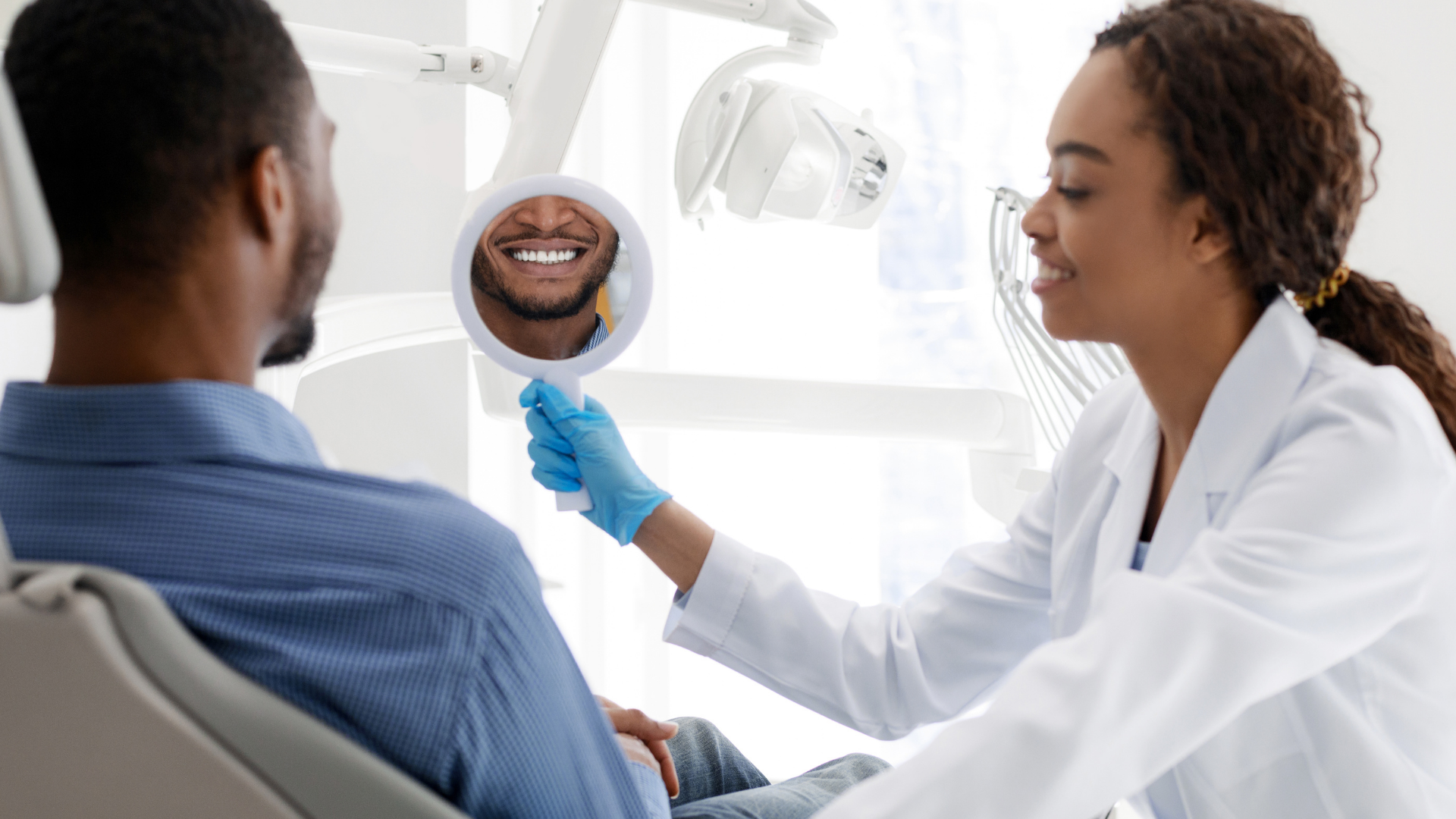 Dentist showing a dental X-ray to a seated patient in a bright clinic.
