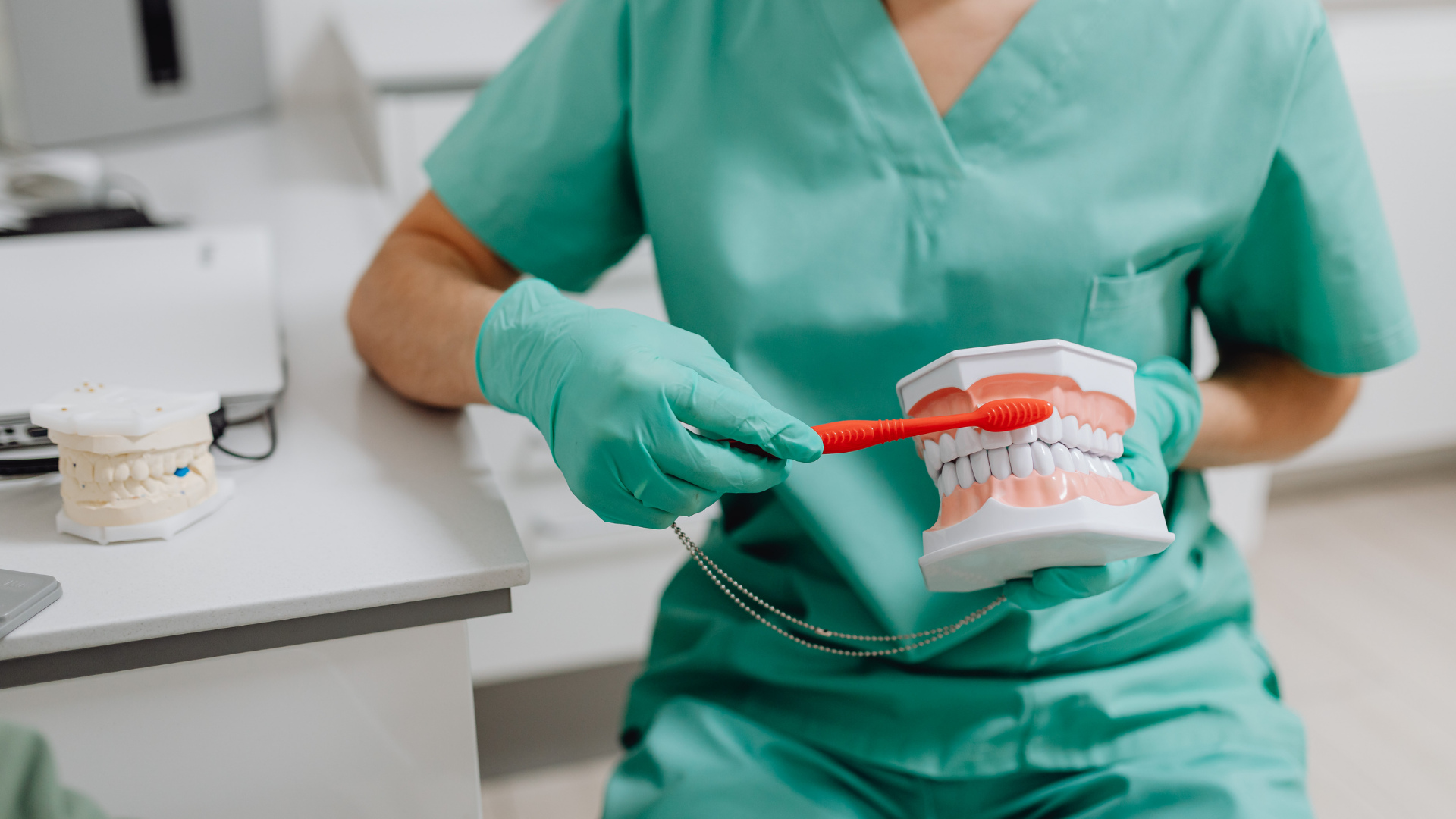 Dental hygienist in green scrubs demonstrating a model of teeth with a toothbrush in a clinic