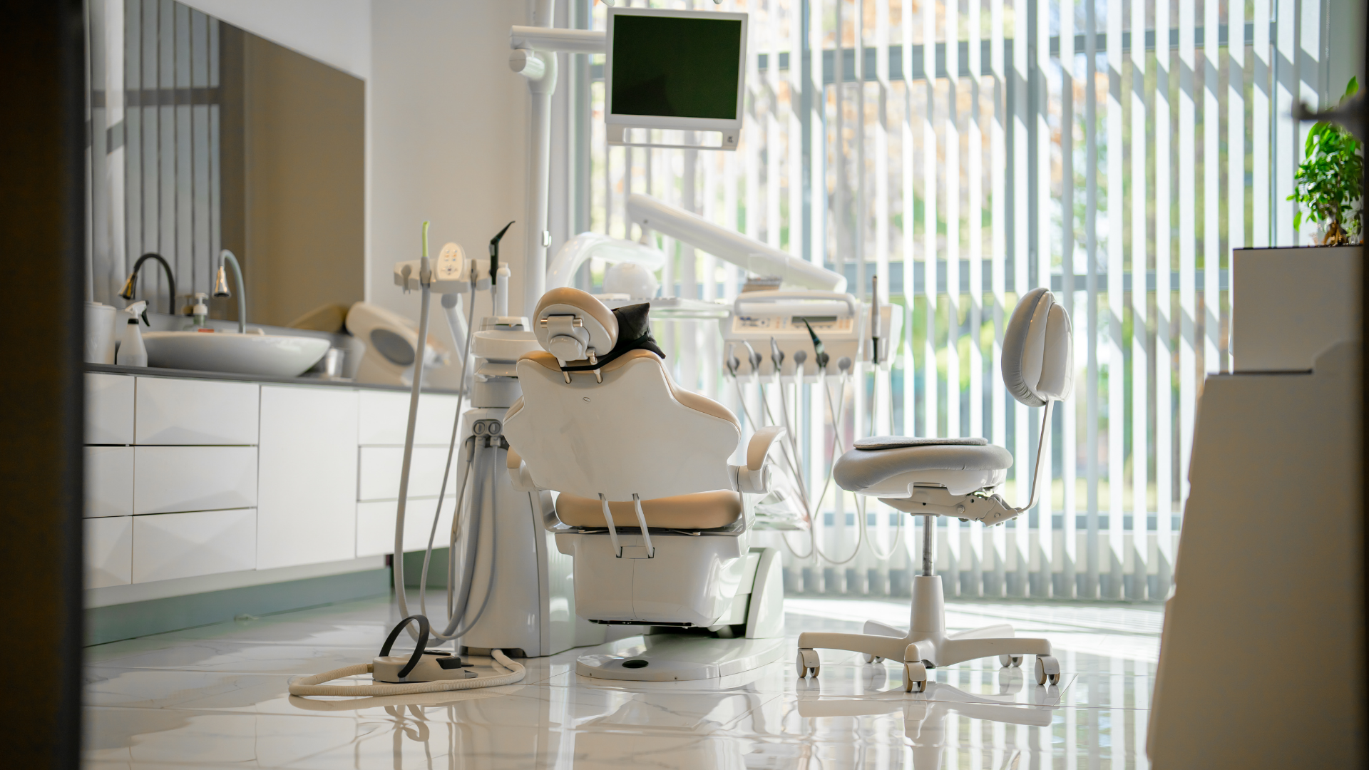 Modern dental office with chair, exam lights, sink, and bright vertical blinds