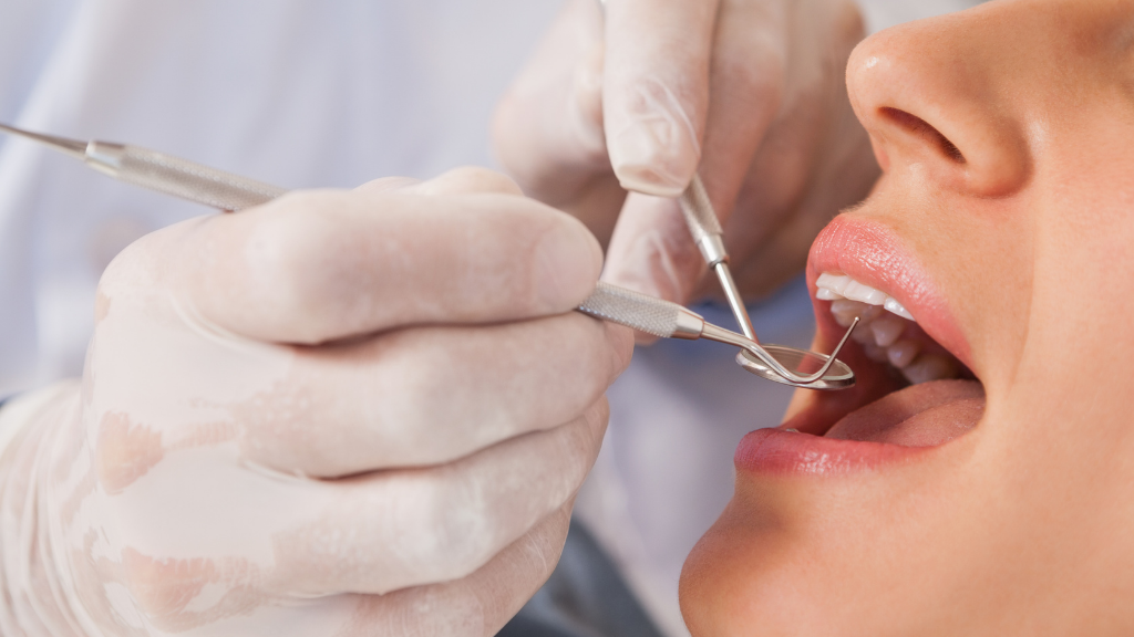 Dentist examining a patient's teeth with dental instruments; close-up view.