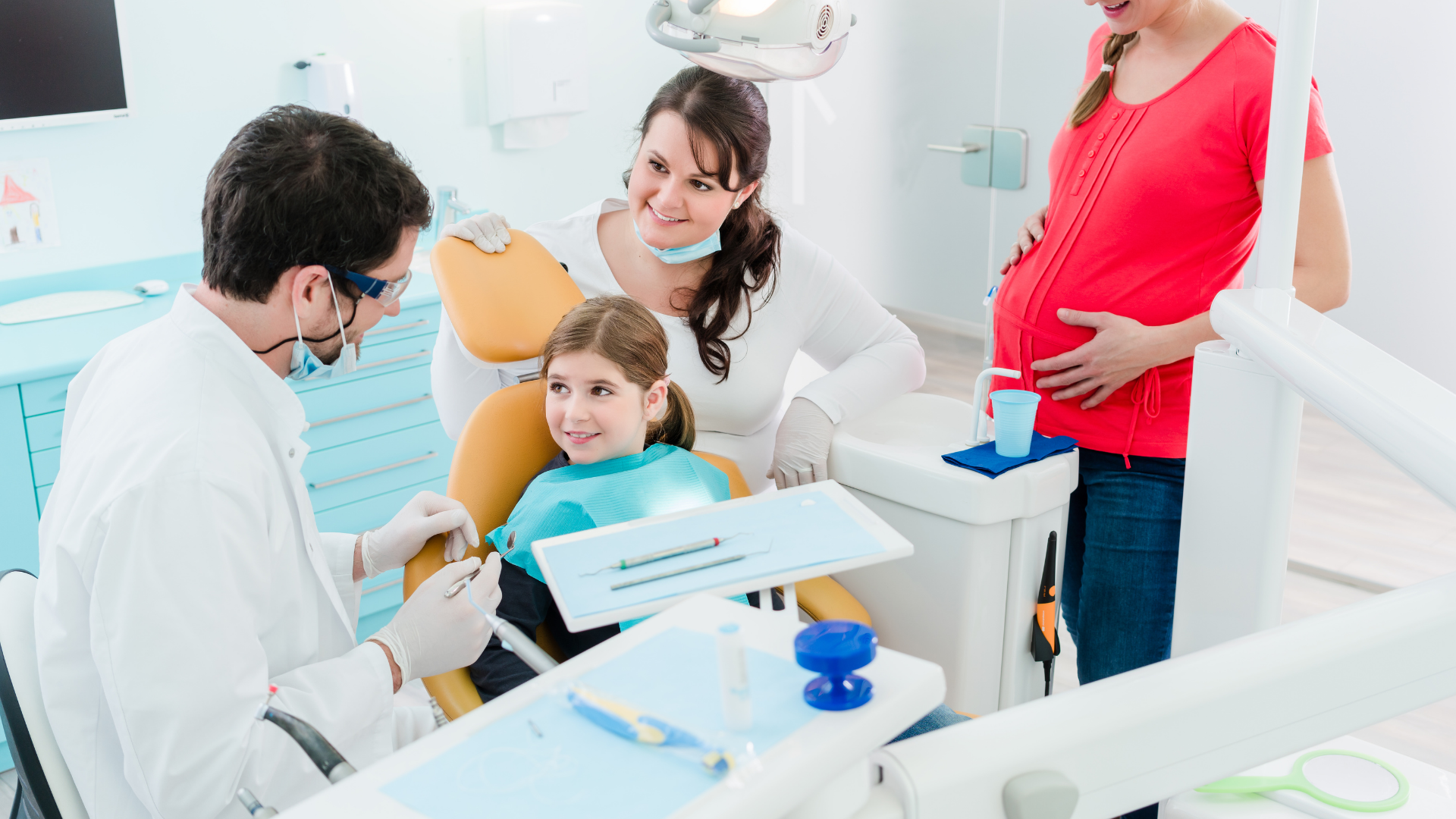 Dentist examining child's teeth; pregnant woman and assistant observe in dental office.