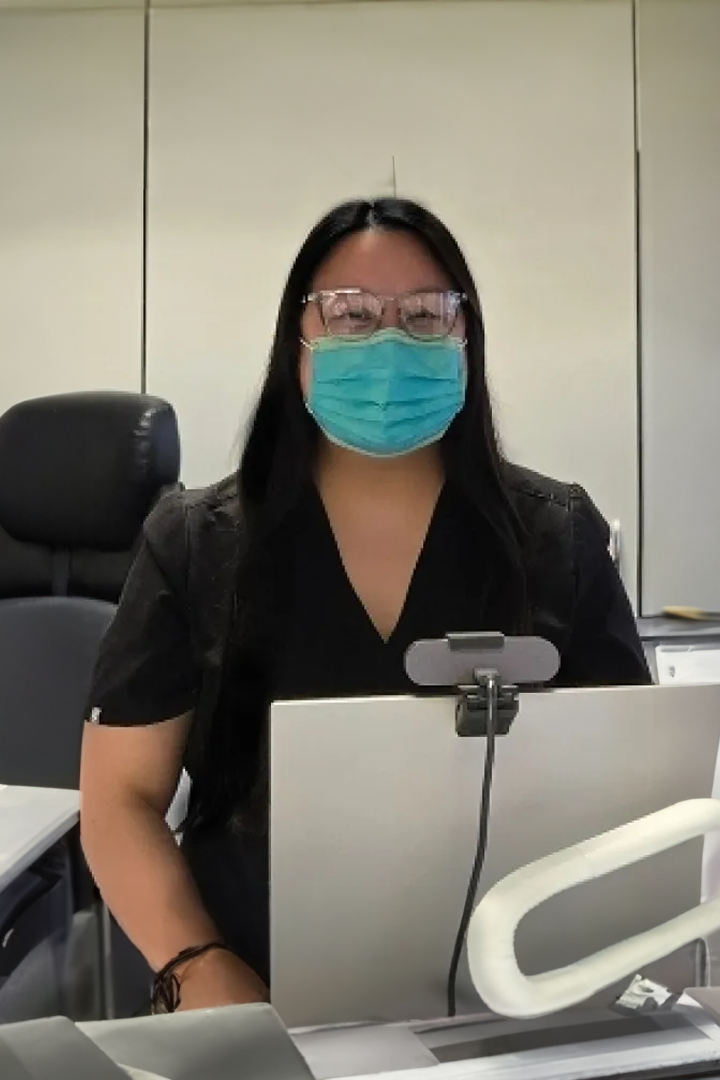 A woman wearing a mask and glasses is sitting in front of a laptop