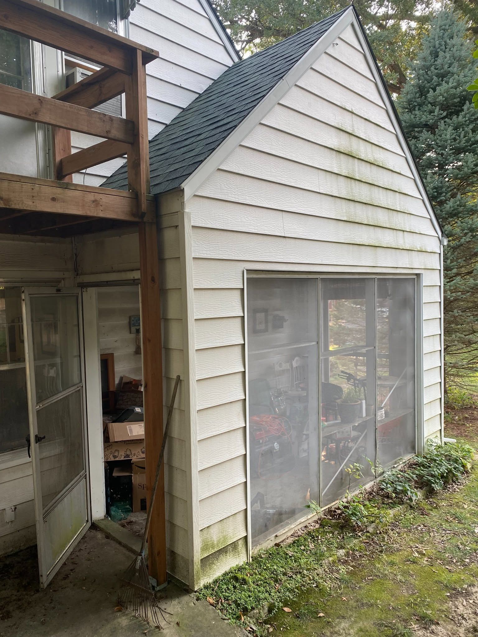 Weathered white shed with screened windows beside a wooden deck and garden greenery