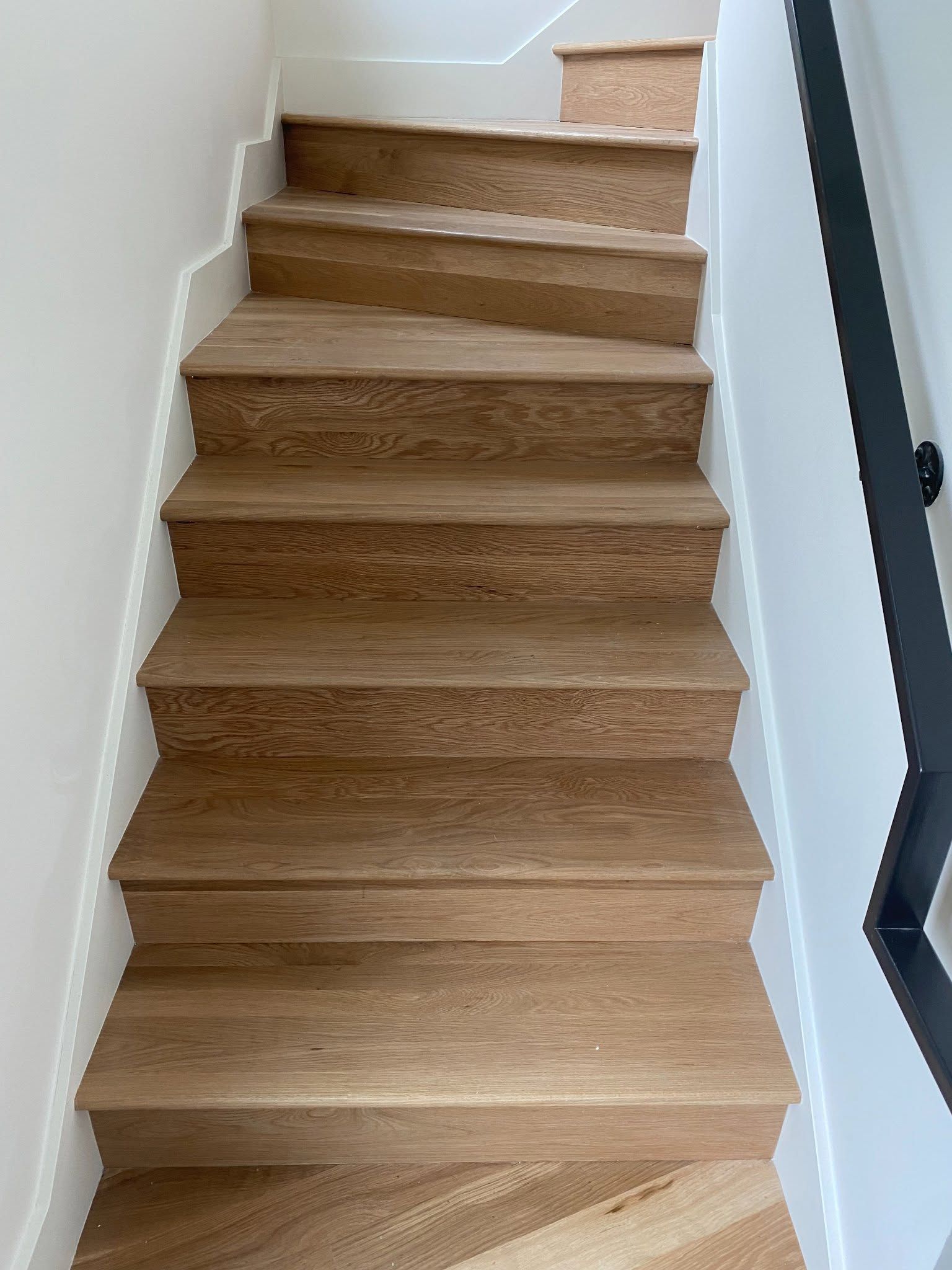 Wooden staircase with carpet runner and white walls, viewed from the bottom looking up