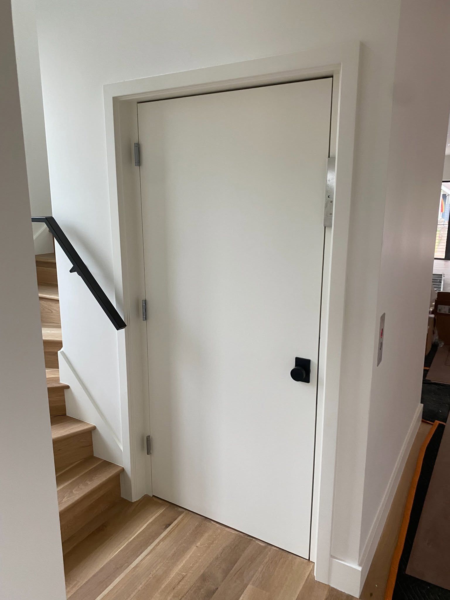 White interior door beside wooden stairs and hallway railing in a home.
