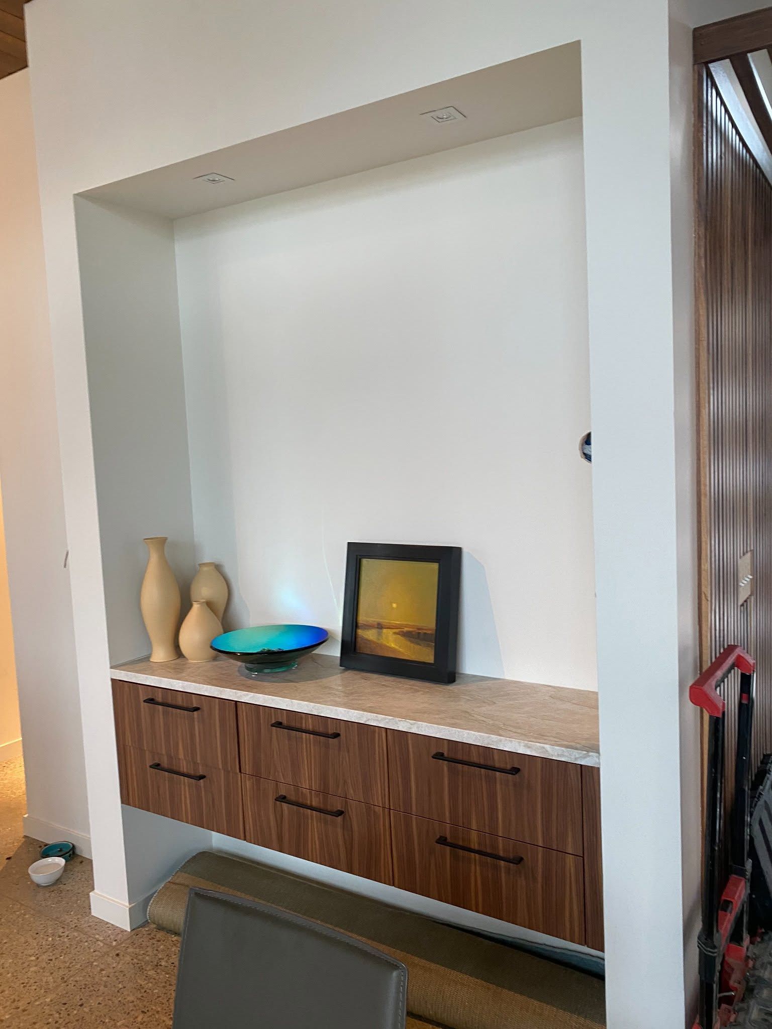 Built-in wooden cabinet with decorative vases and framed art in a recessed wall niche