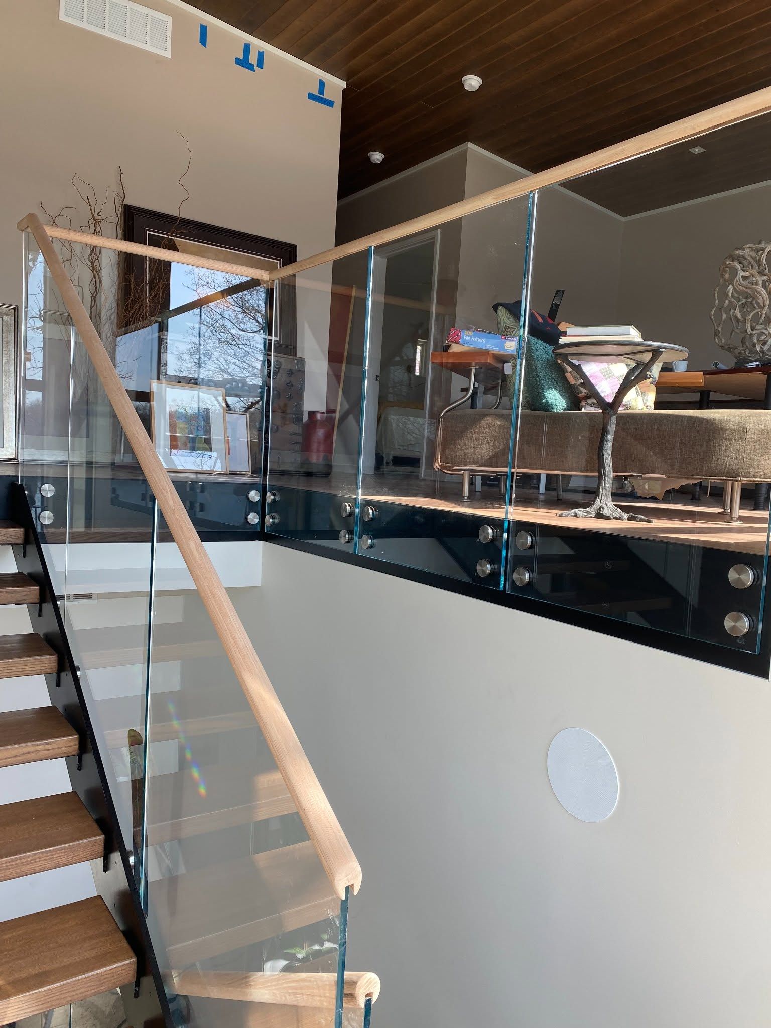 Modern interior with glass staircase, wooden handrails, and a mezzanine seating area