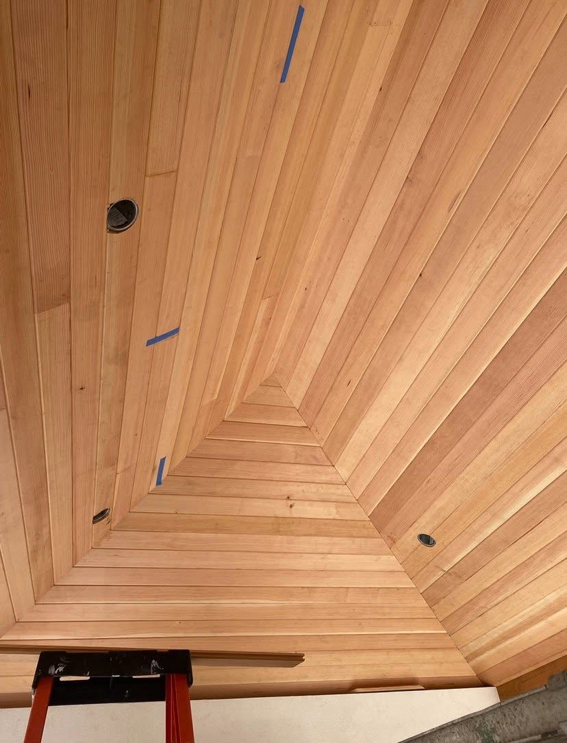 Wooden ceiling corner with chevron panels, dark screw holes, and a small red ladder at the bottom.