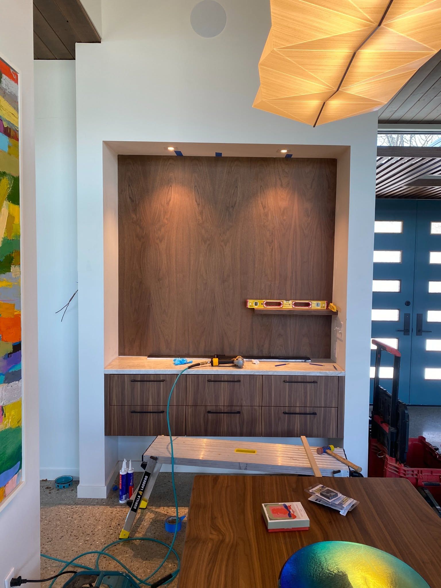 Modern interior with built-in wood shelving, a table in front, and colorful wall art on the left.