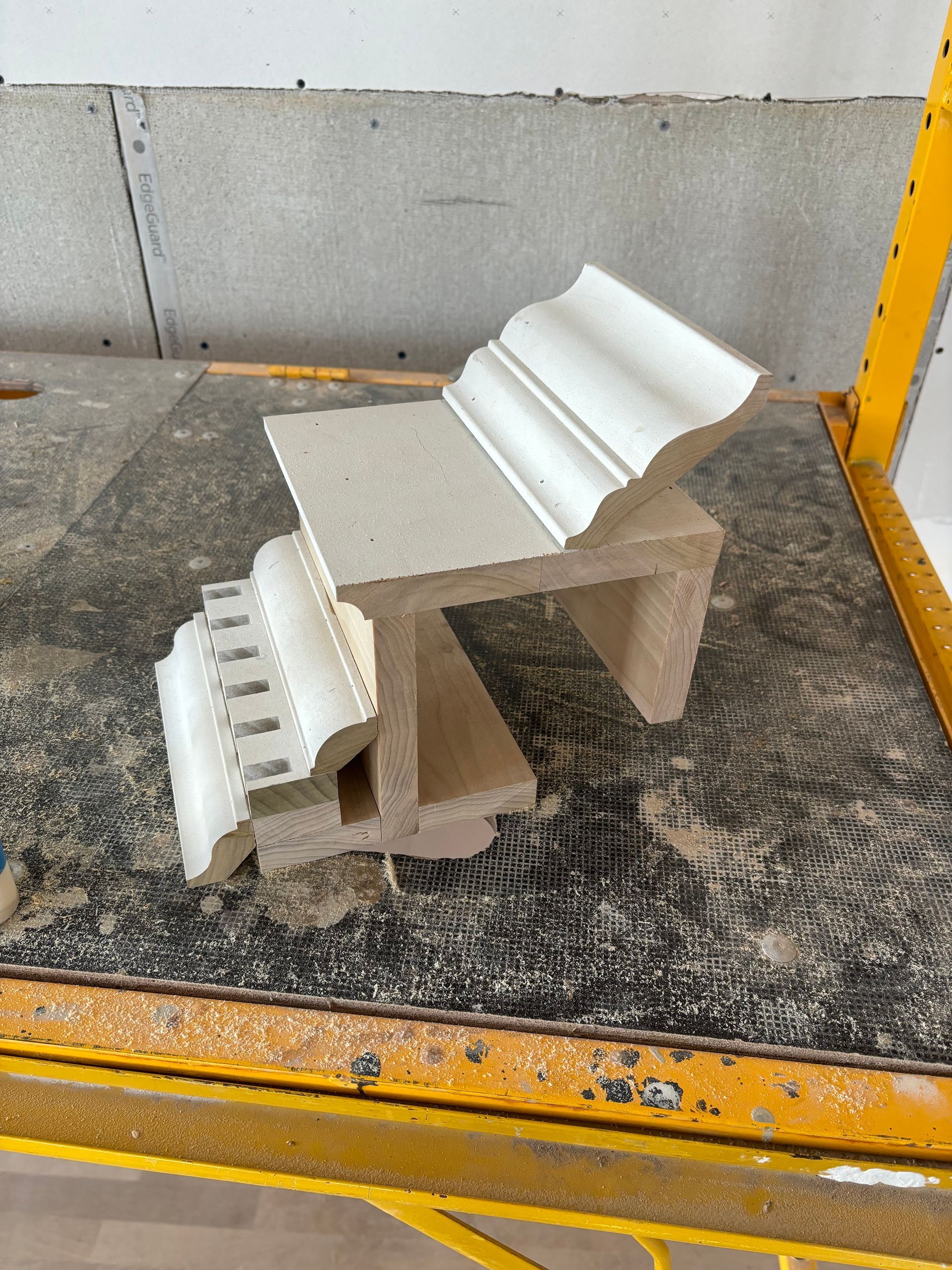 Small gray concrete chair sculpture on a dark mat beside a yellow safety barrier.