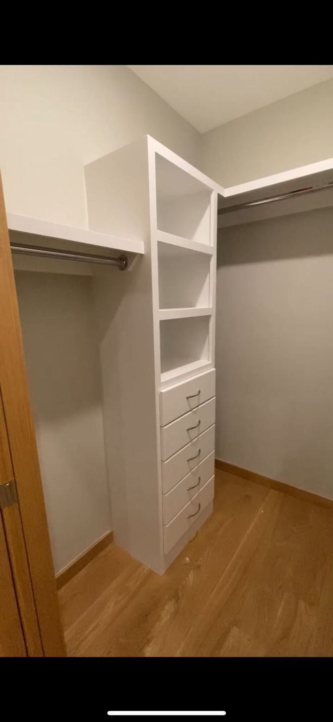 Small walk-in closet with white shelves, drawers, and hanging rods on both sides over a wood floor.