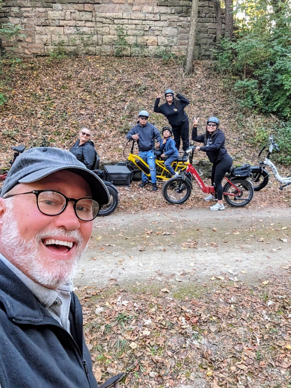 Smiling man in cap takes a selfie with four cyclists and mountain bikes on a wooded trail