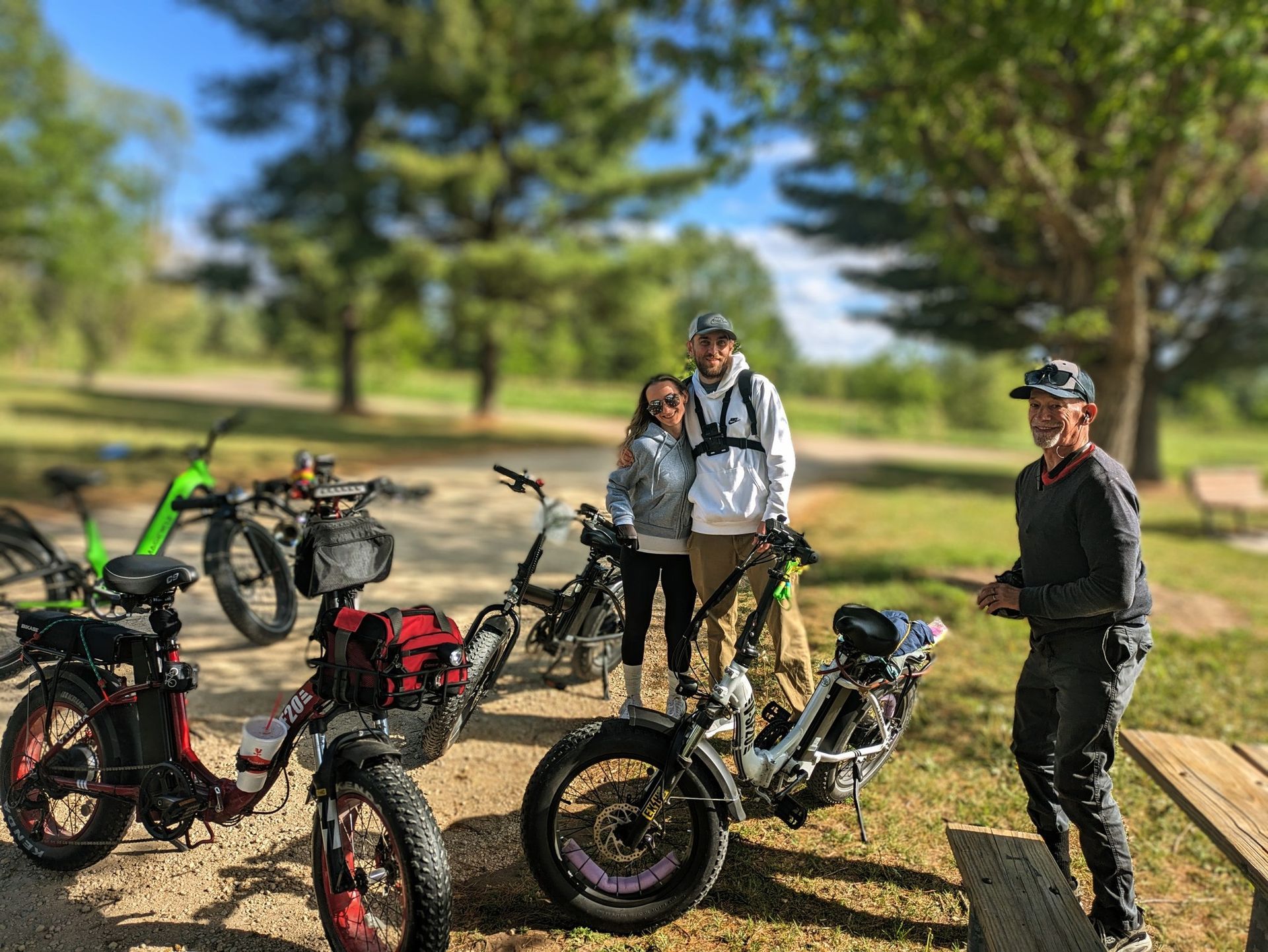 Three cyclists with electric bikes posing on a sunny park trail