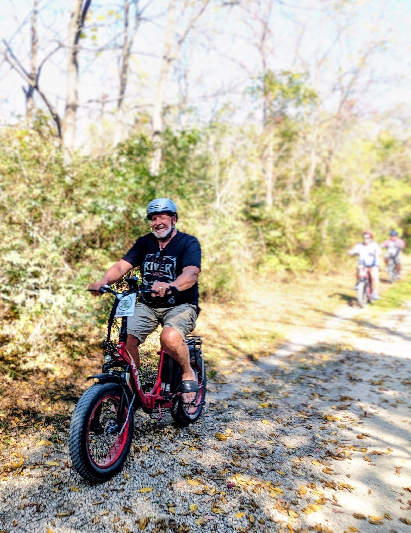 Person riding a red fat-tire bike on a wooded trail in sunlight