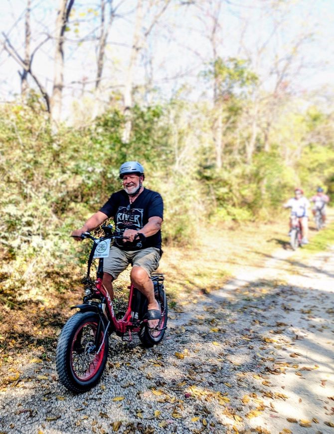 Person riding a red fat-tire bike on a wooded trail in sunlight