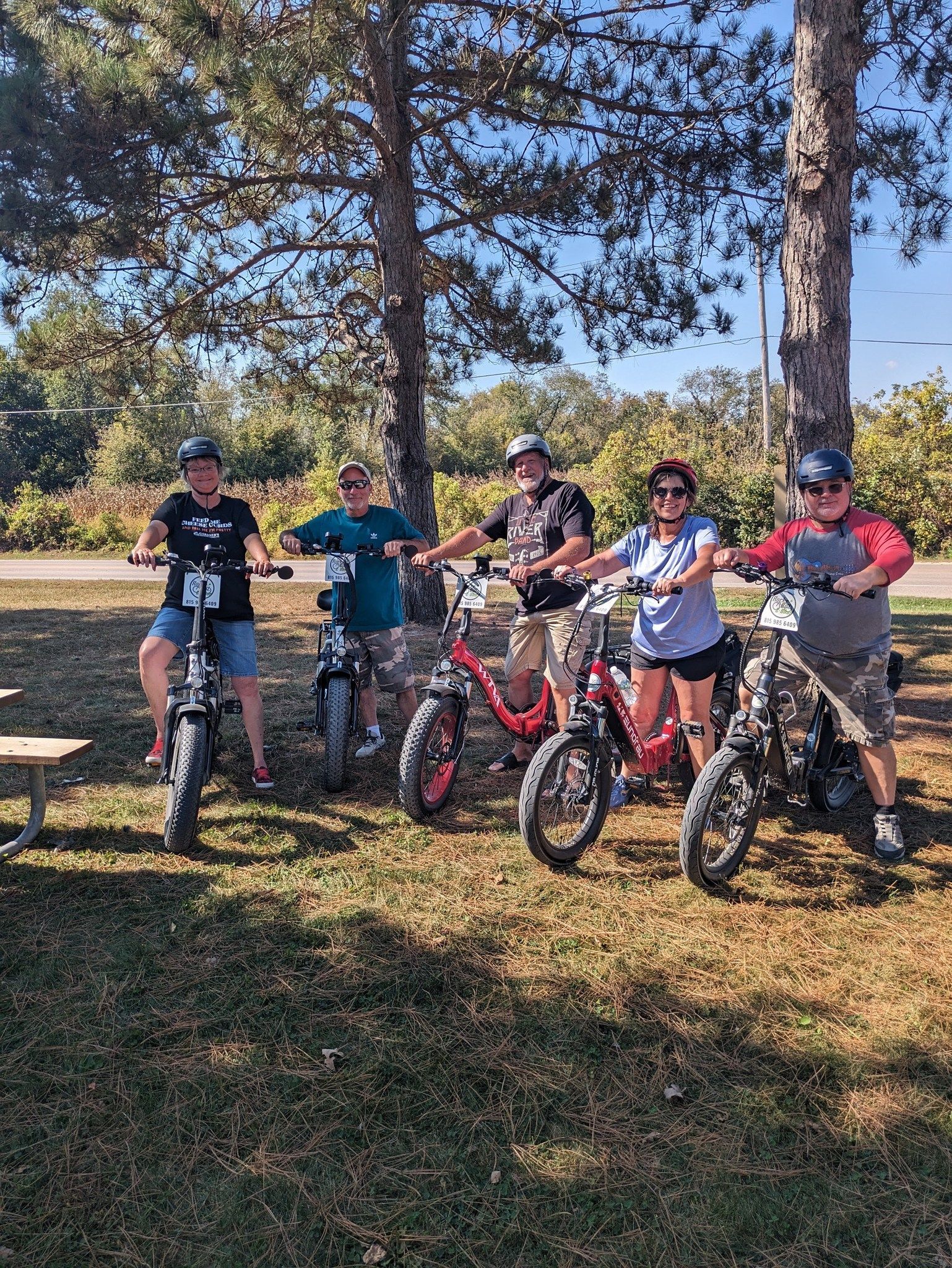 Five kids standing with bikes in a sunny park under tall trees