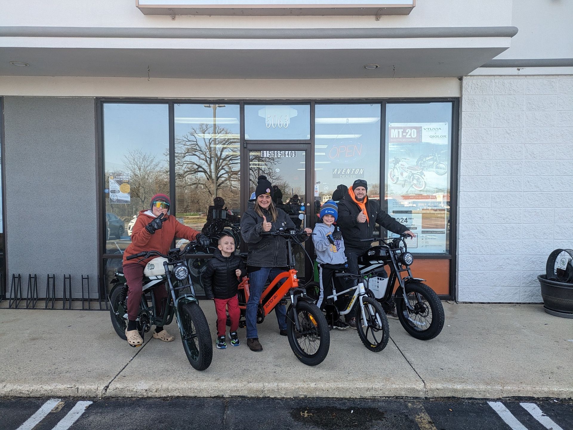 Five people posing with bicycles outside a storefront entrance