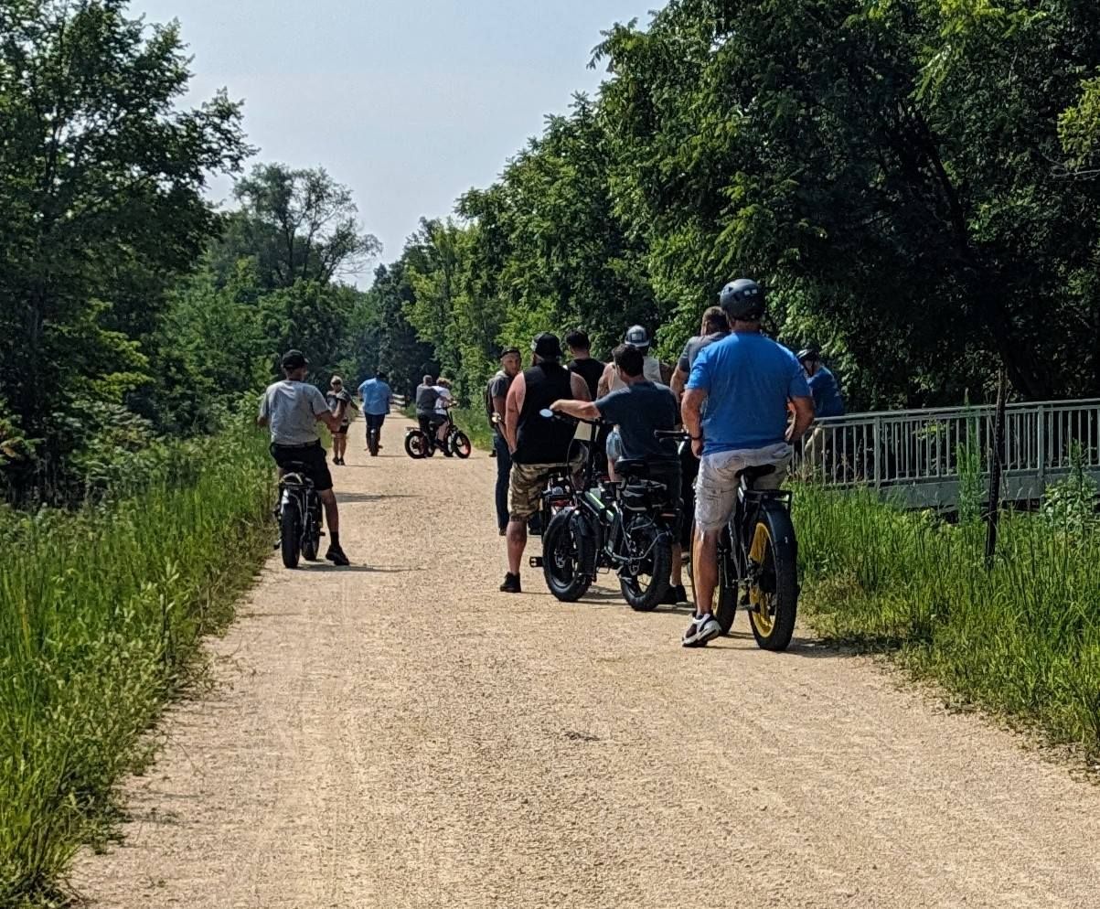 People biking and walking on a gravel trail through green trees on a sunny day